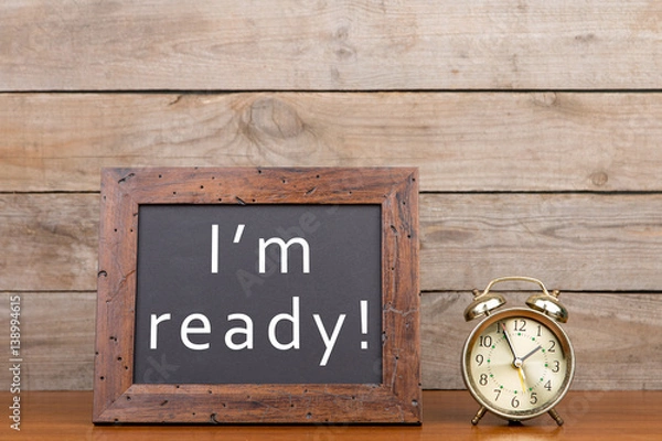 Fototapeta Alarm clock and blackboard with text "I'm ready" on brown wooden background