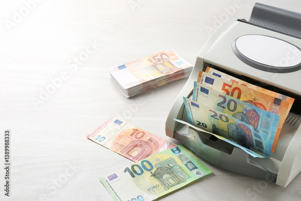 Fototapeta Money counter machine with euro banknotes on white wooden table, closeup. Space for text