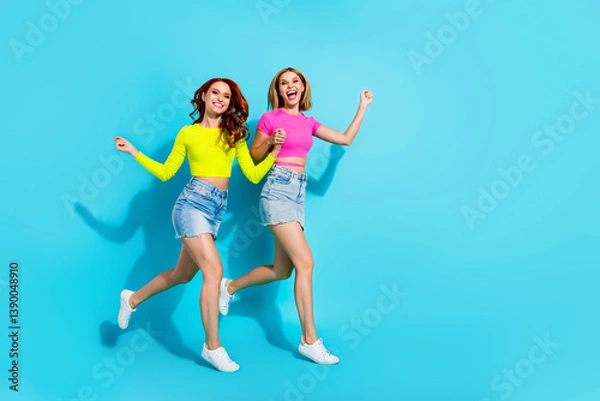 Fototapeta Joyful young women jumping against a bright turquoise background, embracing summer vibes and friendship in colorful outfits