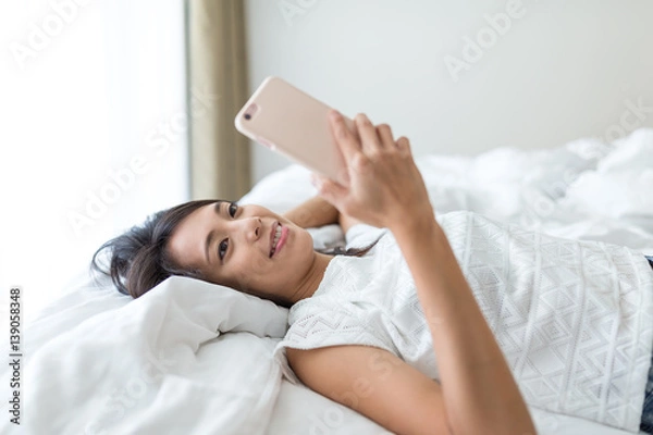 Fototapeta Woman using cellphone and lay down on bed