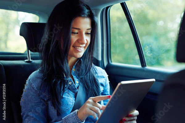 Fototapeta Smiling woman sitting in a car with tablet computer