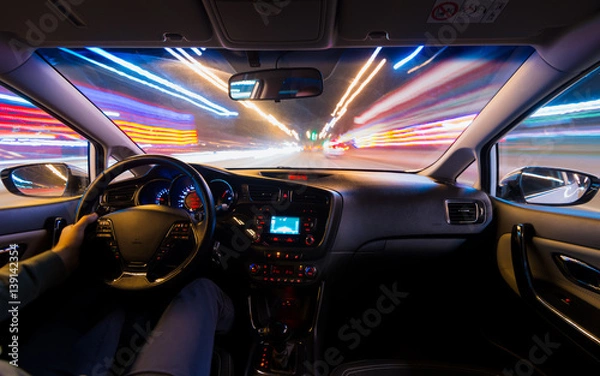 Fototapeta hands on the wheel a car moves at fast speed at the night. Blured road with lights with car on high speed. Car speed night drive on the road in city