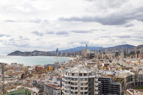 Fototapeta Aerial photo of the Spanish town of Benidorm in Spain showing the old town of the city with the beach known as Platja de Ponent or West Beach Promenade in background as well as mountains and clouds