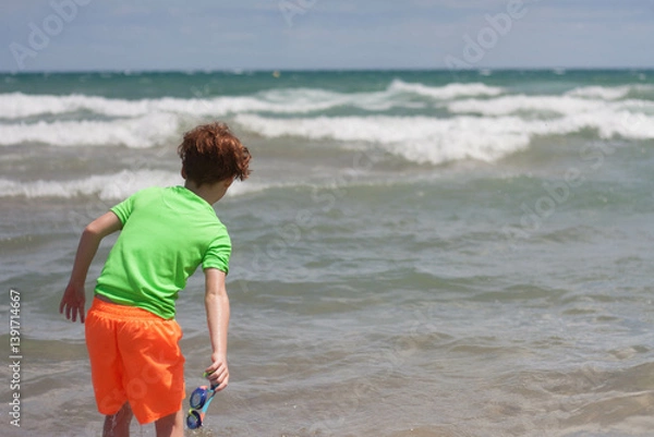 Obraz portrait of redhead boy from behind with orange swimsuit and green t-sirt looking at the sea. Horizontal. copy space