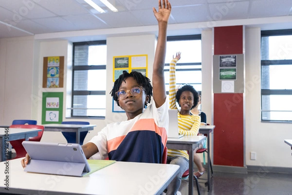 Obraz In school, diverse students raising hands while using tablet in classroom