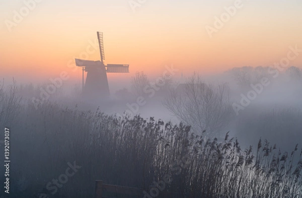 Fototapeta Dawn at a traditional, Dutch windmill in the spring fog.