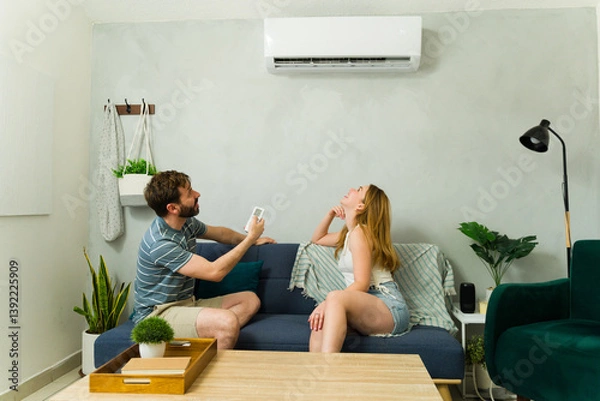 Fototapeta Couple relaxing on sofa using air conditioner remote control during summer heat