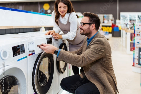 Fototapeta Beautiful and happy middle age couple buying consumer tech products in modern home appliances store. They are choosing washing or cloth dryer machine. People and consumerism concept.