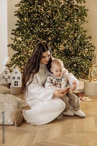 Obraz Mother and son sitting near a Christmas tree with a garland before the New Year and Christmas