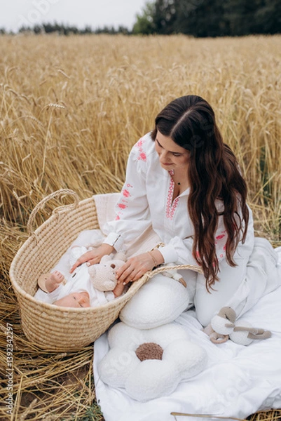 Obraz Mother playing with 1 month old son in crib in wheat field on picnic. Newborn boy