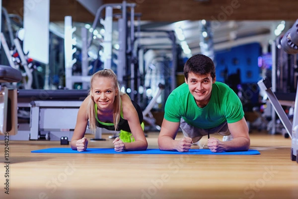 Fototapeta Sport couple doing pushups  bar on floor in the gym.