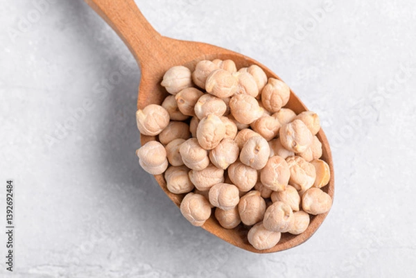 Fototapeta Raw chickpeas on wooden spoon on grey table background. Healthy plant-based protein, healthy cooking ingredient for vegan recipes and vegetarian diets