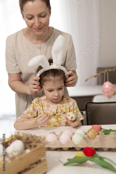 Fototapeta A delightful and joyful moment shared between a mother and her daughter as they decorate colorful Easter eggs at home