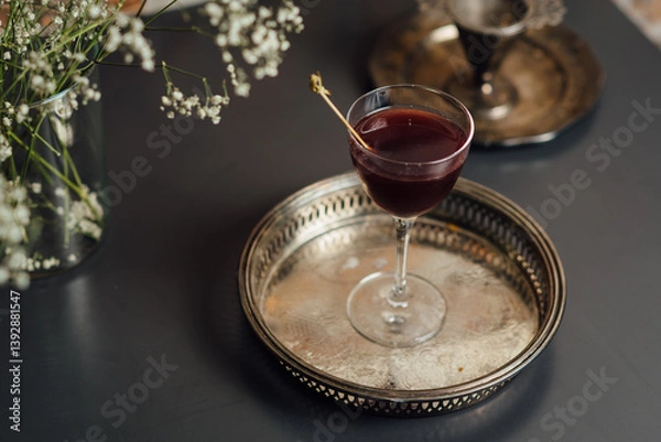 Fototapeta Red cocktail in a stylish glass placed on a decorative metallic tray, complemented by delicate table decor, creating a sophisticated ambiance