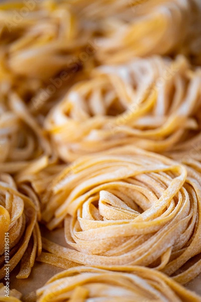 Obraz Freshly made, uncooked pasta nests are closely arranged, showcasing their texture and golden color. The image highlights the intricate details and craftsmanship of homemade pasta, making it appealing 