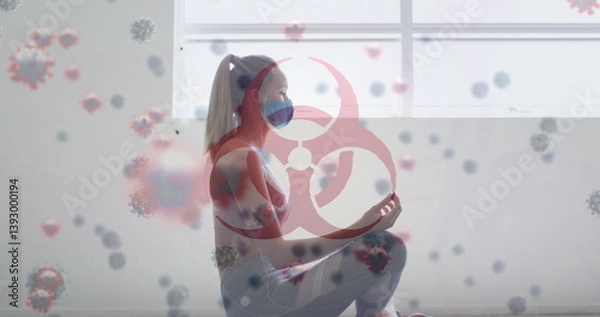 Fototapeta Image of covid-19 cells floating over caucasian woman wearing face mask meditating