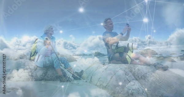 Obraz Caucasian senior couple hiking, taking photo with smartphone, over clouds and network of connections