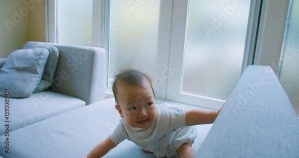 Obraz Curious Asian Baby Exploring Home Environment on Sofa in Bright Living Room with Natural Light with a curious expression.