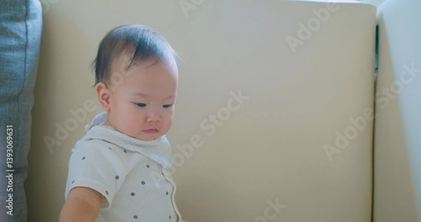 Obraz Cute baby with a curious expression holding a toy wearing a white outfit and scarf sitting indoors.