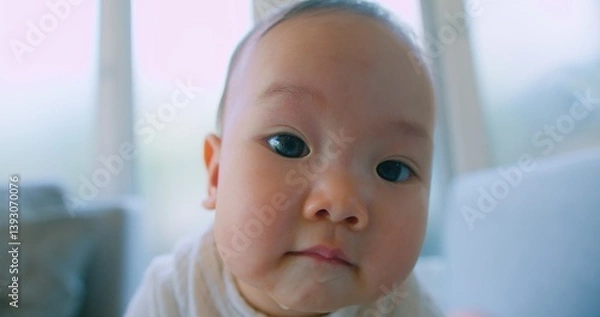 Obraz Close-up of a cute Adorable baby with wide eyes Curious Expression Looking Directly at Camera, capturing a moment of innocence in a well-lit home environment.