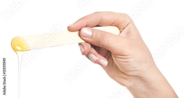 Fototapeta Beauticians hand with green glove holding a roll on liposoluble wax cartridges from honey for waxing wooden spatulas for wax on black. Preparing for epilation