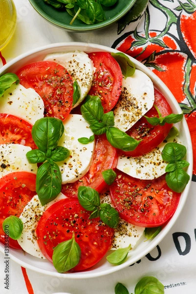 Fototapeta Traditional Italian caprese salad with tomatoes, mozzarella and basil on a white plate