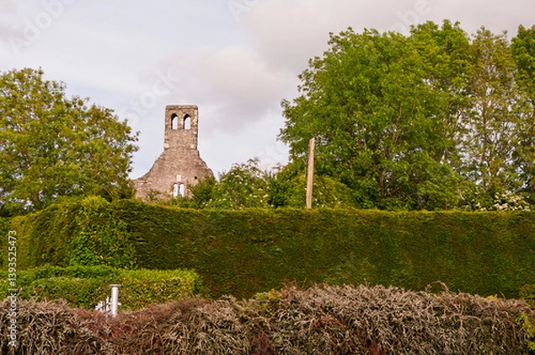 Fototapeta A tall tower with a bell sits in front of a hedge