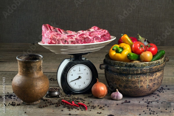 Obraz The meat on the scales, vegetables and pottery on a wooden table