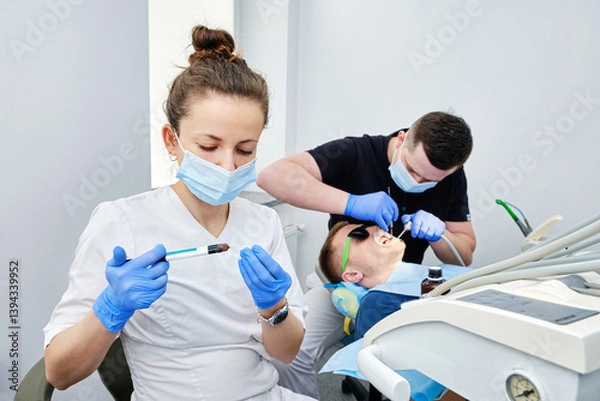 Fototapeta Dentist and Assistant Cementing Crown. Installing a dental crown. Teamwork in Dentistry.