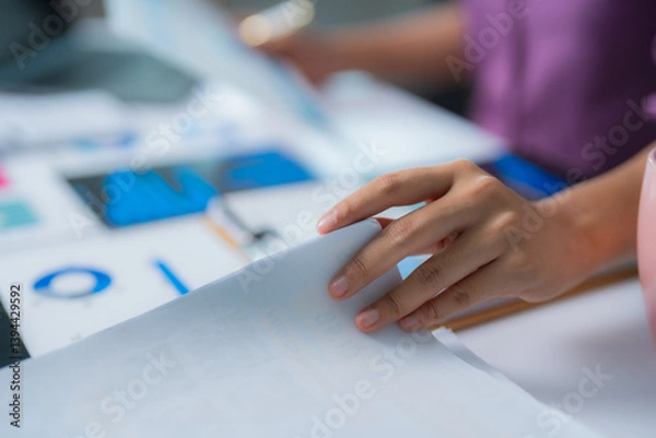 Fototapeta Businesswoman turning page of document while analyzing financial data with charts and graphs, focusing on market trends and investment opportunities