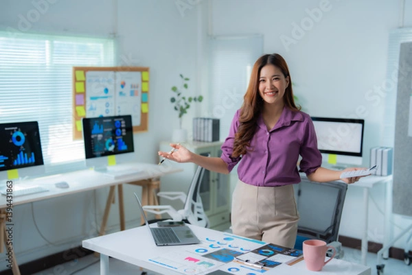 Fototapeta Young successful asian businesswoman presenting marketing data analysis charts smiling in modern office, working with charts and graphs, using a laptop computer and a pen in her hands