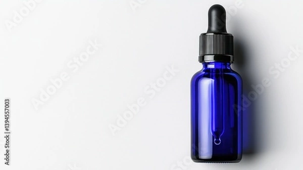 Obraz Blue glass dropper bottle with a black cap, isolated on a white background, showcasing a drop of liquid.
