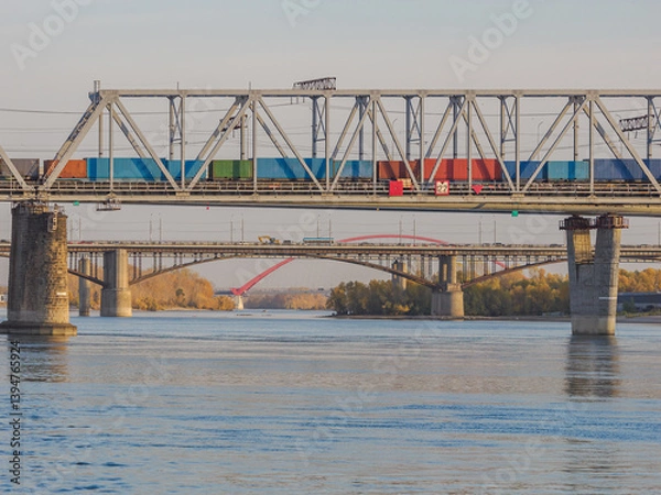 Fototapeta A train carries containers across a river bridge.