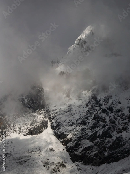Fototapeta Snowy mountain landscape on a cloudy day with the peaks covered with clouds