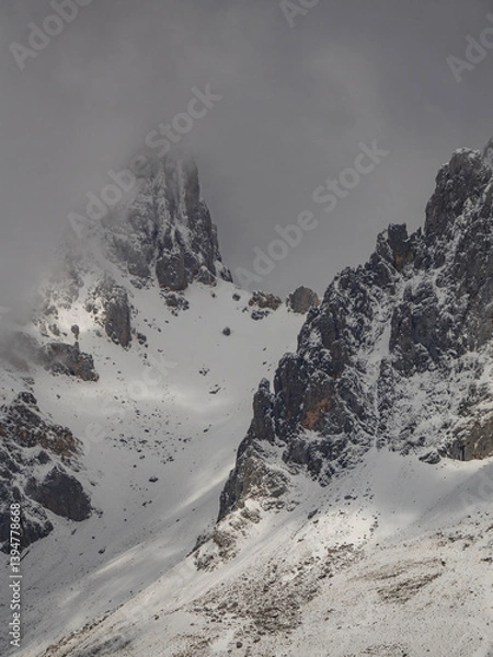 Fototapeta Snowy mountain landscape on a cloudy day with the peaks covered with clouds