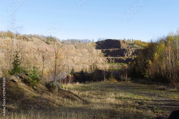 Fototapeta Borówno Mine, Poland - a landscape featuring a former quarry with exposed rock faces, a body of water at the bottom, and surrounding autumn foliage under a clear sky