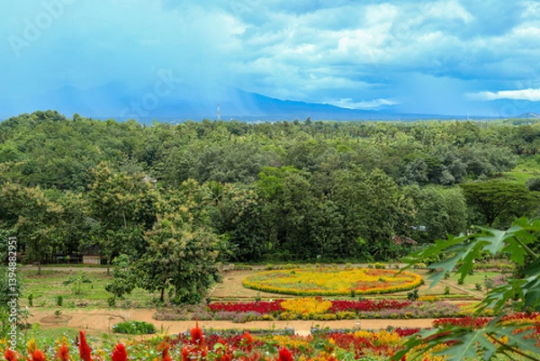 Obraz Colorful flower garden with lush greenery and mountain backdrop. High-angle view of a vibrant flower garden with various colorful flowers arranged in intricate patterns.