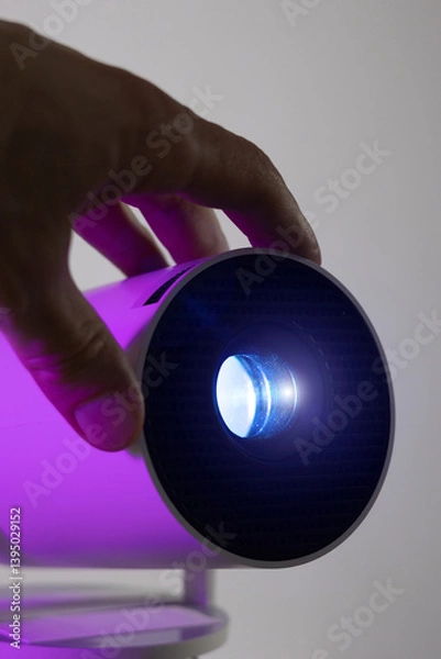 Obraz Vertical photo of man's hand adjusting of lens modern wi-fi video-projector with lighting blue light. Video or photo presentation and home movie watching.