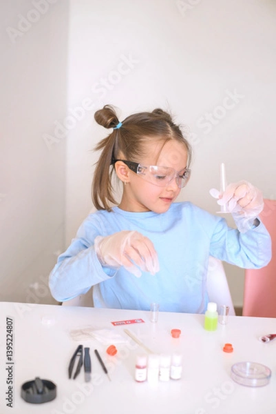 Obraz A child wearing gloves and goggles does a scientific test experiment with a test tube and liquids