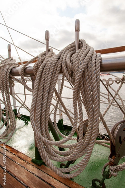 Fototapeta Nautical ropes neatly coiled around belaying pins on a sailing ship. Marine rigging details with textured ropes, metal, and wood, evoking maritime craftsmanship and seafaring tradition...