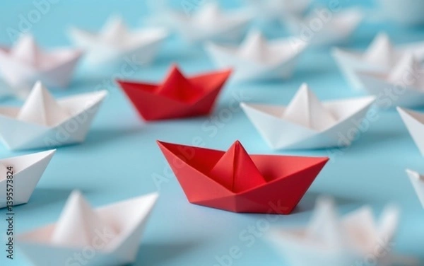 Obraz A vibrant red origami boat stands out among white ones on a blue background, creating a striking visual contrast