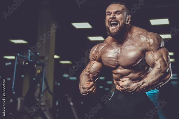 Fototapeta Handsome fit caucasian muscular man flexing his muscles in gym