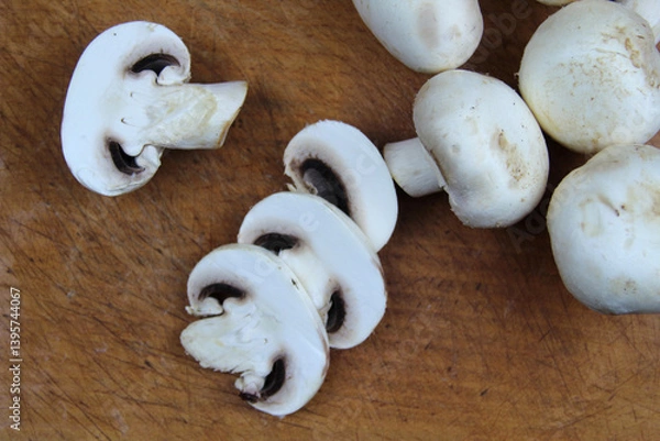 Fototapeta Sliced ​​mushrooms lie on a wooden board, in the background are whole large champignons