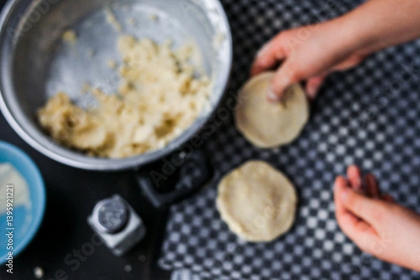 Obraz Blurred image of hands taking arepa (colombian food) from table with pot, bowls and utensils, portraying culinary preparation.