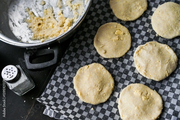 Obraz Arepa (colombian food) on table with pot, bowls and utensils, portraying culinary preparation.
