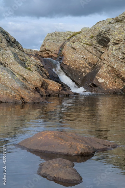 Fototapeta A serene photo of a small waterfall flowing between rocky cliffs into a calm pool.
