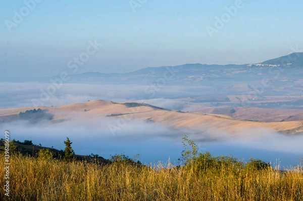 Fototapeta Panorama visto dal crinale che scende da R adicofani lungo la Via Francigena con la bruma mattutina che taglia in due le colline