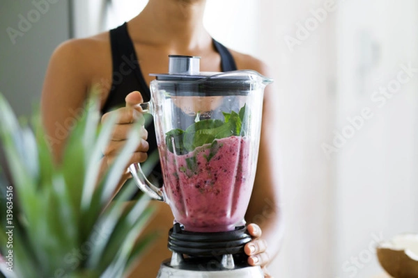 Obraz Woman blending spinach, berries, bananas and almond milk to make a healthy green smoothie