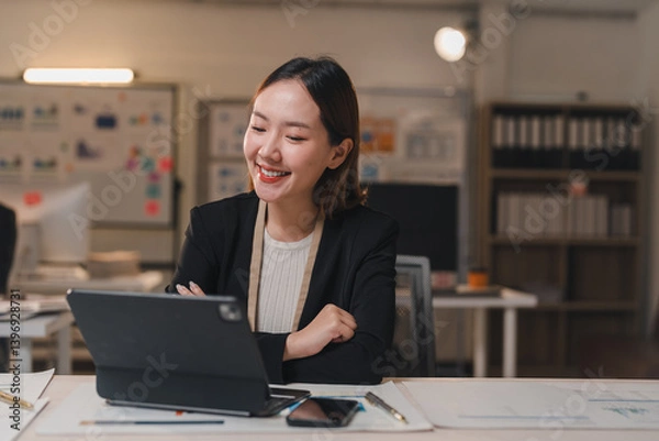 Obraz Young professional woman using tablet and working late at night, enjoying her job and smiling while looking at the screen in a modern office
