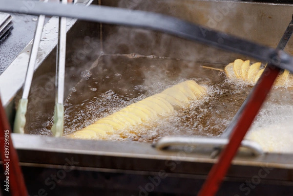 Fototapeta Potatoes in the form of a spiral on a wooden skewer begins lowered into boiling vegetable oil.